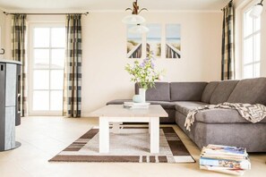 Una sala de estar con un sofá, una mesa de centro con un jarrón de flores, una estantería y vista al mar a través de la ventana.