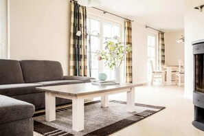 Una sala de estar con sofá, una mesa de centro, chimenea y un área de comedor al fondo.