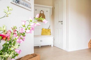Un pasillo con una puerta blanca, un banco y una bolsa amarilla, y un cartel en la pared.