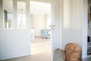 Ein Zimmer mit einer Tür zu einem Wohnbereich, einem hellblauen Sofa und einer braunen Tasche auf dem Boden.