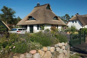 A traditional thatched-roof house with a stone wall in front, surrounded by greenery and a parked car. - Holiday home with 2 bedrooms (Fuhlendorf)
