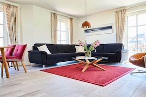 A modern living room with a black sofa, a red rug, and a glass coffee table. - Holiday home with 2 bedrooms (Fuhlendorf)
