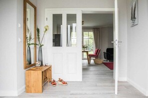Een gang met een houten console tafel, een spiegel en een deur die leidt naar een kamer met een rode stoel en een tafel.