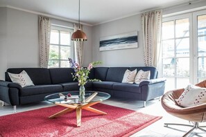A modern living room with a dark sofa, a glass coffee table, and a red rug. - Holiday home with 2 bedrooms (Fuhlendorf)
