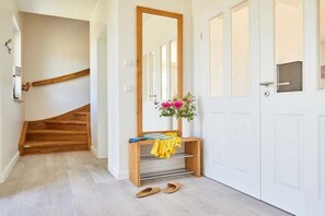 A hallway with a wooden staircase, a mirror, a bench with a vase of flowers, and a pair of shoes on the floor. - Holiday home with 2 bedrooms (Fuhlendorf)