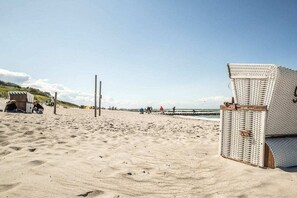 A beach with a wicker chair, a wooden post, and a distant view of the sea. - Holiday home with 2 bedrooms (Fuhlendorf)