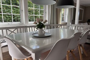 A dining area with a white table and chairs, a vase with flowers, and a window with greenery outside. - Holiday home in Bastorf with swimming pool (Bastorf)