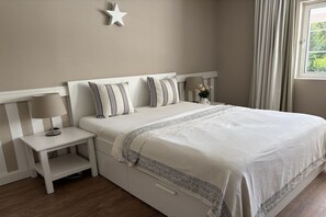 A bedroom with a bed, bedside table, lamp, and a window with curtains. - Holiday home in Bastorf with swimming pool (Bastorf)