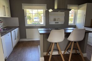 A kitchen with a central island, two white chairs, a window with a view, and built-in cabinets. - Holiday home in Bastorf with swimming pool (Bastorf)