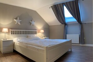 A bedroom with a sloped ceiling, a bed with white bedding, two bedside lamps, and a window with curtains. - Holiday home in Bastorf with swimming pool (Bastorf)