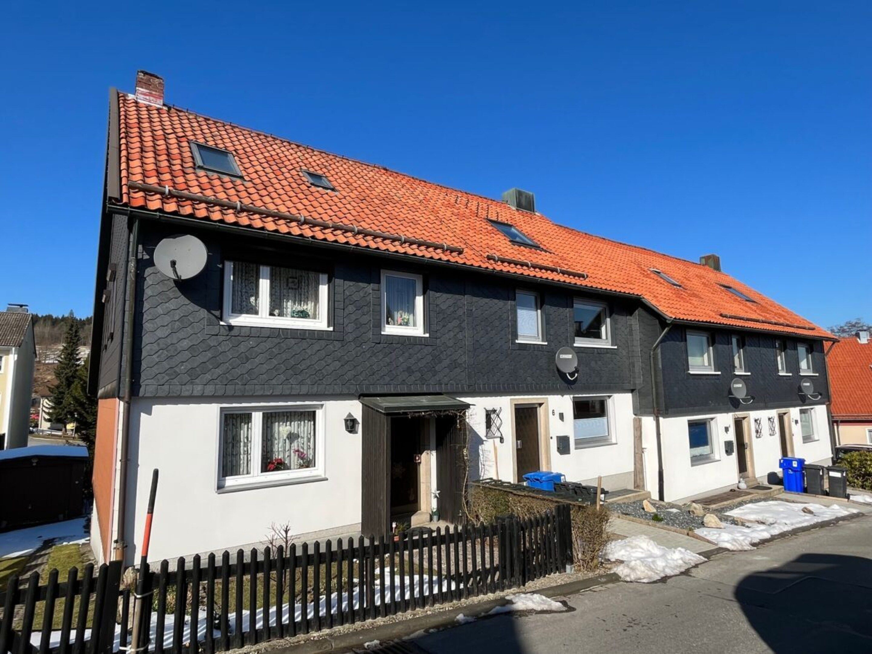 A two-story residential building with a red-tiled roof, white and dark grey exterior walls, and a black fence in front.