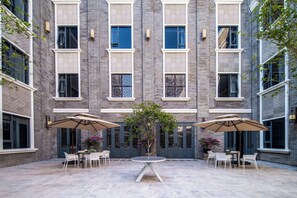 Un patio con una mesa redonda y sillas, rodeado de muros de ladrillo y amplias ventanas.