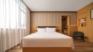 A hotel room with a large bed, a chair, and a wooden floor. - Shili Huating Hongpu Hotel (Guangzhou)
