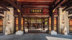 A traditional building entrance with a dark wooden roof, a sign with golden characters, and two stone lion statues on either side. - Shili Huating Hongpu Hotel (Guangzhou)