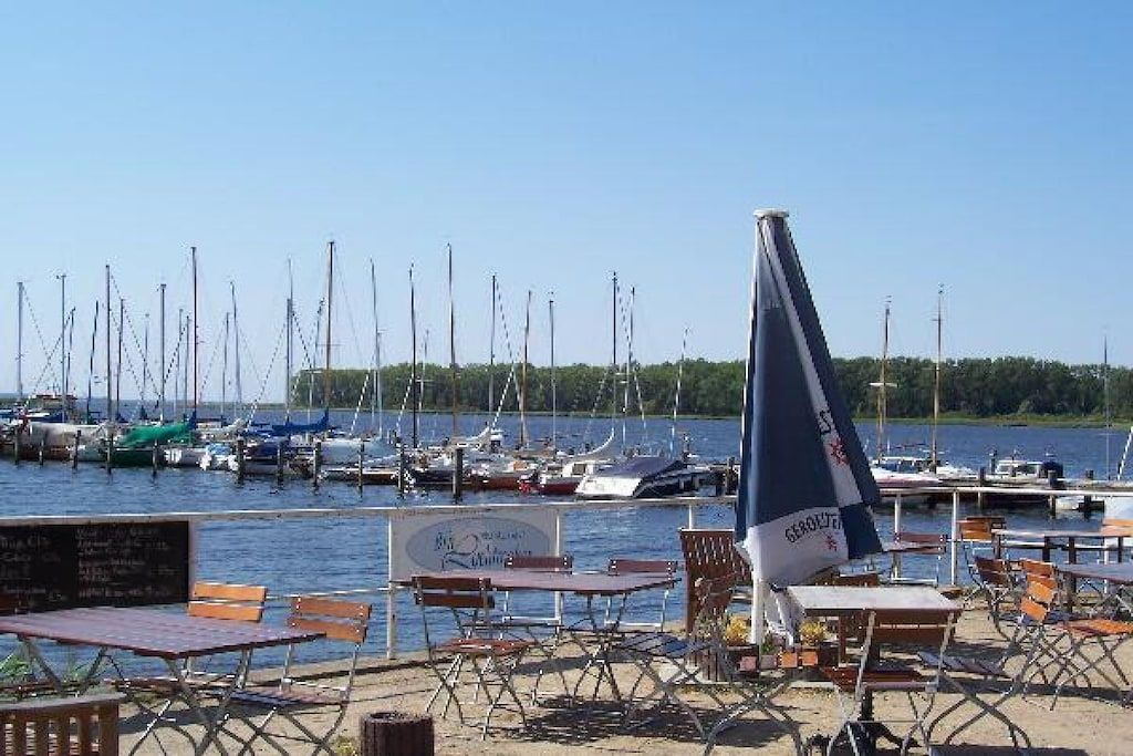 A marina with boats docked, outdoor seating, and a clear sky.