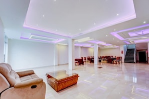 A spacious hotel lobby with a seating area, a reception desk, and a staircase leading to another floor.