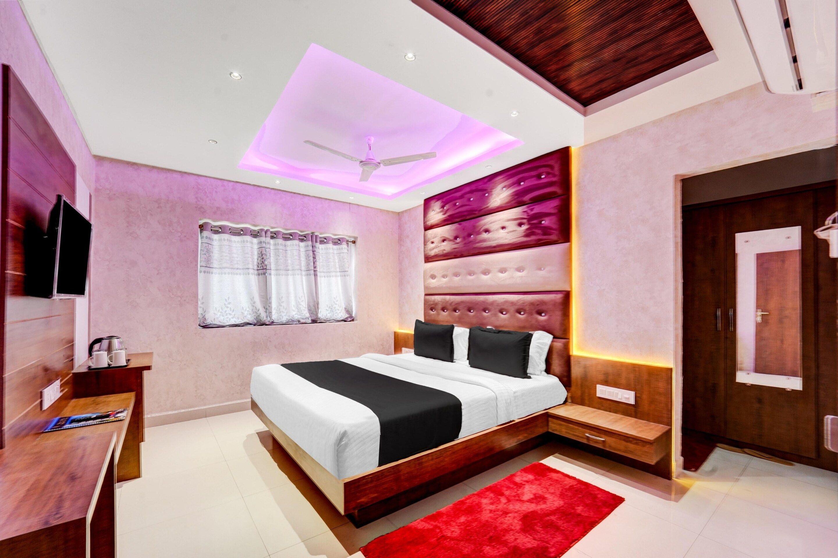 A modern bedroom with a bed, a desk, a TV, and a red rug.
