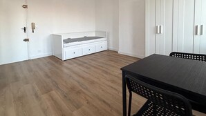 Ein Zimmer mit Holzboden, einem weißen Bett, einem weißen Kleiderschrank und einem schwarzen Tisch mit Stühlen.
