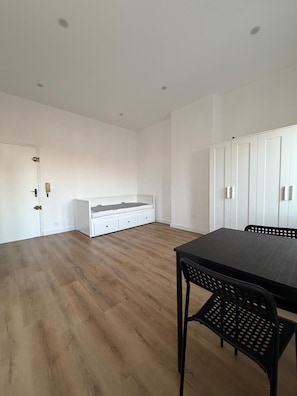 A room with a wooden floor, a white bed, a white wardrobe, and a black table with chairs. - Vrbo Property (Marseille)