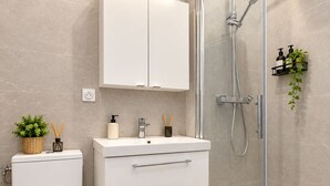 Ein modernes Badezimmer mit Toilette, Waschbecken mit Spiegel, Duschkabine und einem Schrank über dem Waschbecken.