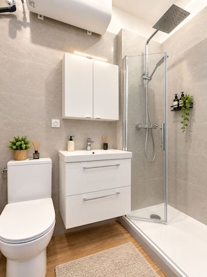 A modern bathroom with a toilet, a sink with a mirror, a shower enclosure, and a cabinet above the sink. - Vrbo Property (Marseille)