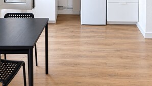Eine kleine Küche mit weißen Schränken, einer Holz Arbeitsplatte, einem kleinen Kühlschrank und einem Fenster mit Tageslicht.