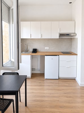 A compact kitchen with white cabinets, a wooden countertop, a small refrigerator, and a window providing natural light. - Vrbo Property (Marseille)