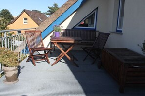 Ein Balkon mit Holztisch, zwei Stühlen, einem Blumentopf und einer Holzbank.