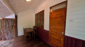 Um corredor com porta de madeira, janela e uma pequena mesa.
