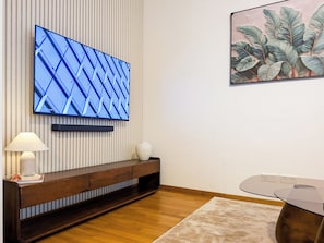 A modern living room with a flat-screen TV mounted on a striped wall, a wooden console table with a vase, a lamp, and a glass coffee table. - Premium Smart Studio near Frauenkirche - 2 Beds - Parking - by RIHOME (Dresden)