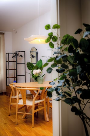 A dining area with a wooden table and chairs, a hanging light fixture, and a potted plant.