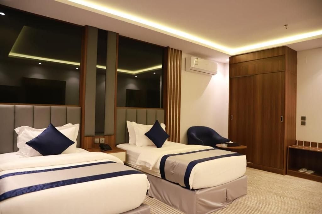 A hotel room with two beds, a wooden wardrobe, a small desk, and a chair.