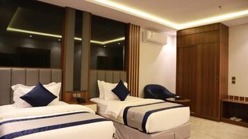 A hotel room with two beds, a wooden wardrobe, a small desk, and a chair.
