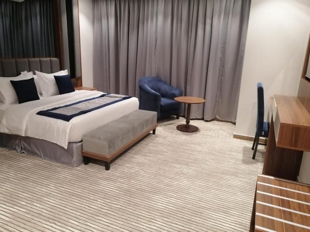 A hotel room with a bed, a chair, a small table, and a wooden desk.