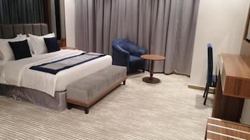 A hotel room with a bed, a chair, a small table, and a wooden desk.
