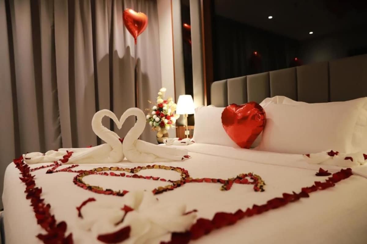 A hotel room with a bed adorned with rose petals and a heart-shaped decoration.