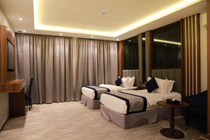 A hotel room with two beds, a desk, a chair, a round table, and a large window. - Tulip View Hotel (Khamis Mushait)