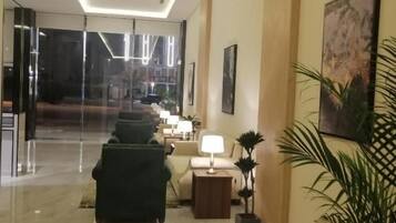 Vestíbulo de hotel con entrada por puerta de vidrio, zona de estar con lámpara y planta en maceta.