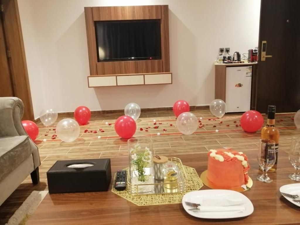 Una habitación con piso de madera, un televisor de pantalla plana montado en la pared, una pequeña kitchenette y una mesa de comedor con un pastel y vasos.