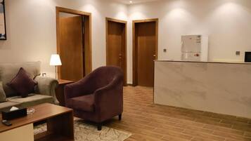 Una camera d'albergo con divano, poltrona, un tavolino, una lampada e un frigorifero.