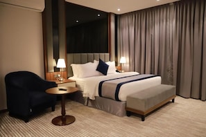 A hotel room with a large bed, a bedside table, a chair, and a lamp. - Tulip View Hotel (Khamis Mushait)