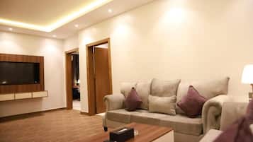 Una sala de estar moderna con un televisor de pantalla plana montado en la pared, un sofá color beige con cojines, una mesa de centro de madera y una puerta que da a otra habitación.