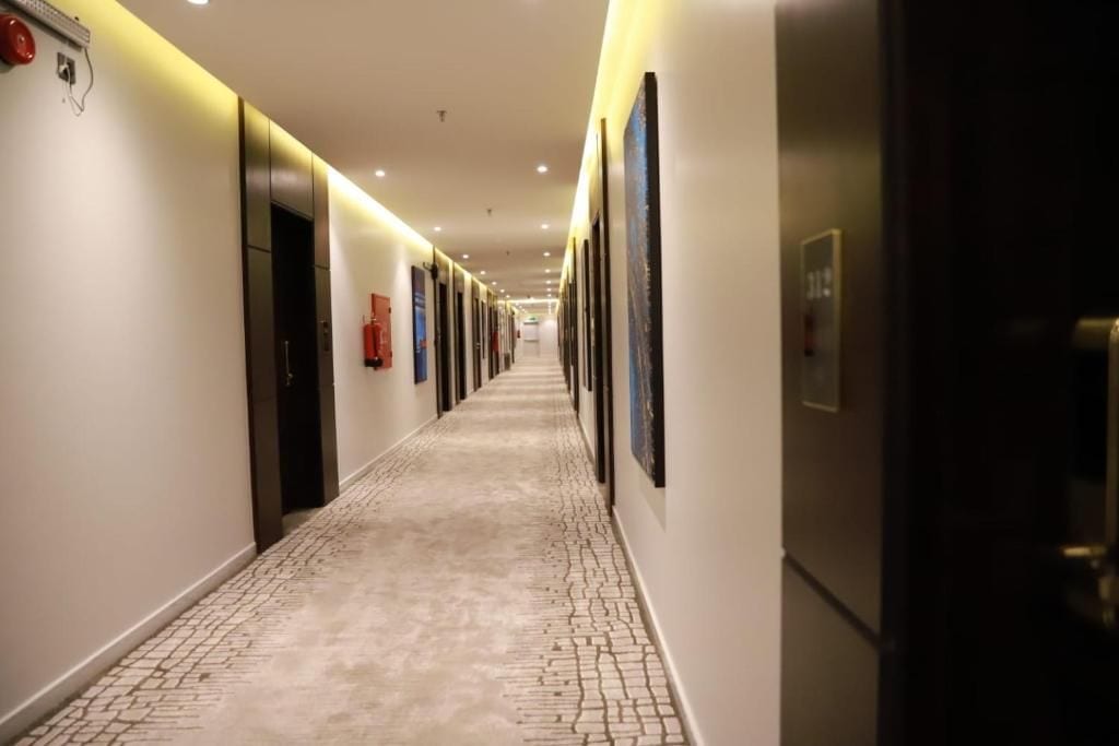 Pasillo de hotel con suelo de baldosas, puertas y cuadros en las paredes.