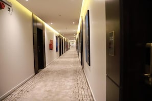 A hotel corridor with a tiled floor, doors, and framed artwork on the walls. - Tulip View Hotel (Khamis Mushait)