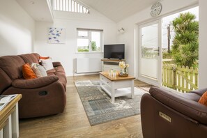 Ein Wohnzimmer mit braunem Sofa, einem Couchtisch, einem Fernseher und Blick ins Freie.