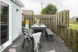 Eine Terrasse im Freien mit Tisch und Bänken, einem Holzzaun und einem Haus im Hintergrund.