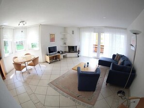 Ett rymligt vardagsrum med en soffgrupp, en TV, en öppen spis och en matplats med stolar och ett bord.
