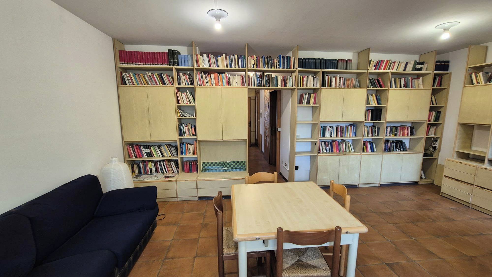 Ein Zimmer mit einem Holztisch und Stühlen, einem dunkelblauen Sofa und mehreren Bücherregalen voller Bücher.