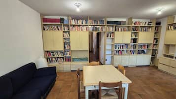 Ein Zimmer mit einem Holztisch und Stühlen, einem dunkelblauen Sofa und mehreren Bücherregalen voller Bücher.