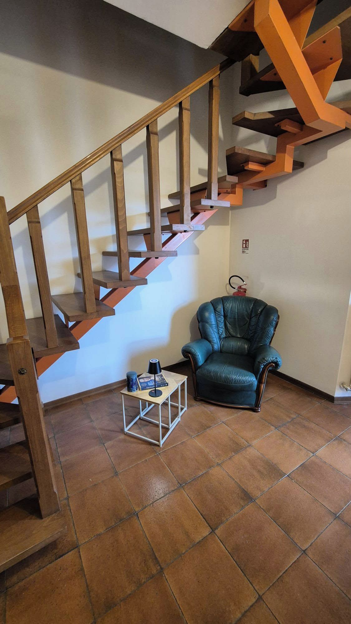 Una scala con ringhiere in legno conduce a una piattaforma. Una poltrona in pelle è posizionata sulla piattaforma, e un tavolino con una lampada si trova nelle vicinanze.